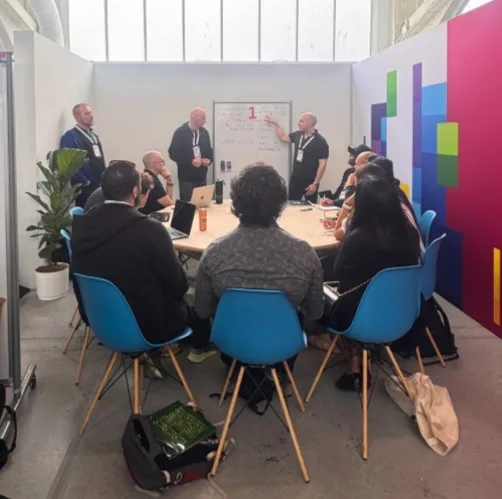 Attendees participate in an interactive table talk session, gathered around a whiteboard discussion focused on multi-tenant application architecture. Azure experts lead conversations on tenant-aware design, migration strategies, and architectural tradeoffs while participants collaborate, ask questions, and share real-world experiences.